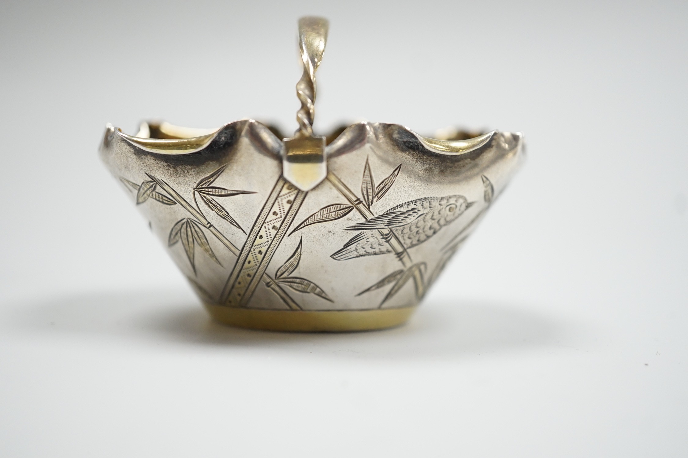 A late Victorian novelty parcel gilt silver salt modelled as a basket, with aesthetic engraved decoration, London, 1884, length 65mm, together with an Egyptian white metal small dish.